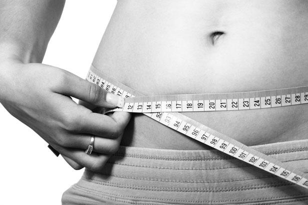 A tape measure positioned horizontally around the abdomen to assess central adiposity and cardiometabolic risk alongside BMI.